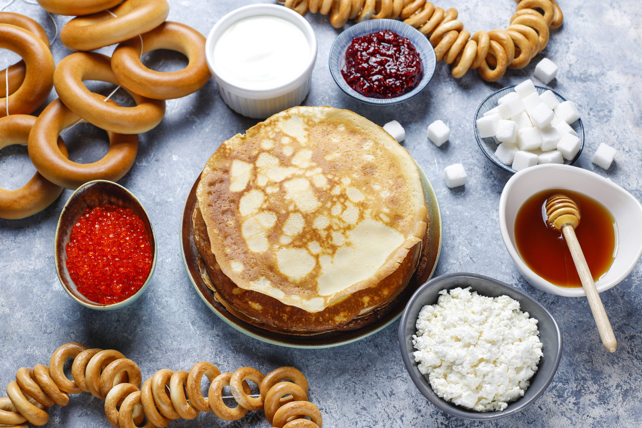 Shrovetide Maslenitsa festival meal. Russian pancake blini with raspberry jam, honey, fresh cream and red caviar,sugar cubes,cottage cheese,bubliks on light background